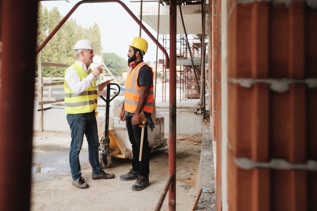 People working in construction site. Men at work in new house inside apartment building. Teamwork with foreman giving instructions to manual worker with forklift.